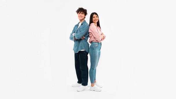 Happy Young Couple Posing Standing Back To Back Smiling To Camera Over White Background. Full Length Shot Of Boyfriend And Girlfriend Expressing Positive Emotions. Youth And Friendship. Panorama - 写真・画像