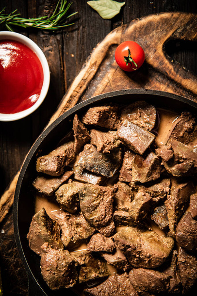 Fried liver in a frying pan on a cutting board with tomato sauce. On a wooden background. High quality photo - Fotó, kép