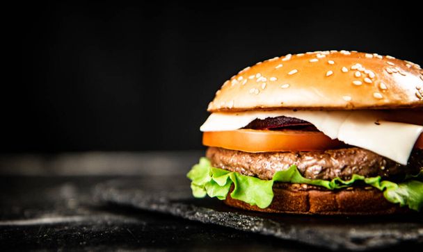 A burger on a stone board on a table. On a black background. High quality photo - Фото, изображение