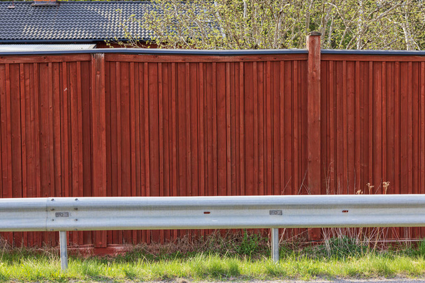 Pohled na červený dřevěný plot a kachlovou střechu obytné budovy za ním. Švédsko.  - Fotografie, Obrázek