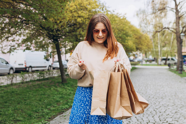 Happy young redhead woman holding shopping paper bags in hands, walking at city street, black friday. Urban lifestyle concept. Delivery carrying. - Zdjęcie, obraz
