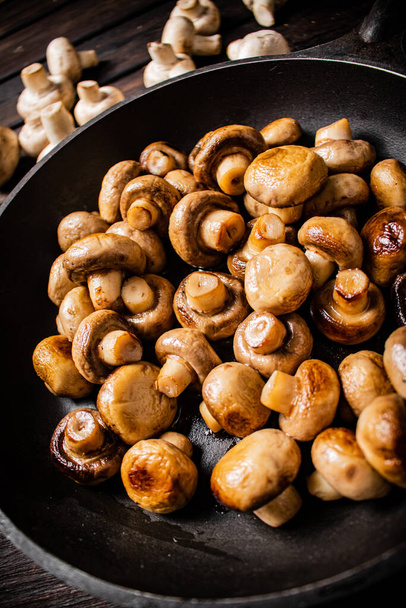 Delicious small fried mushrooms in a frying pan. On a wooden background. High quality photo - Fotoğraf, Görsel