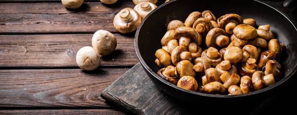 Fragrant homemade fried mushrooms in a frying pan on a cutting board. On a wooden background. High quality photo - Фото, изображение