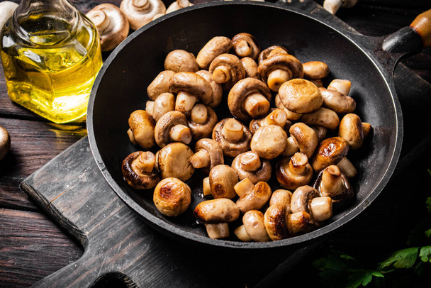 Fragrant homemade fried mushrooms in a frying pan on a cutting board. On a wooden background. High quality photo - Photo, Image