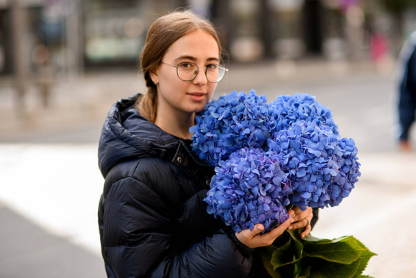 Portrait view of attractive girl florist gently holding large bouquet of fresh hydrangea flowers in blue colors - Фото, изображение