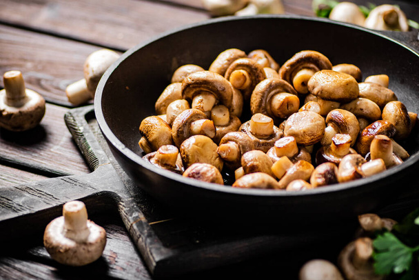Fragrant homemade fried mushrooms in a frying pan on a cutting board. On a wooden background. High quality photo - Foto, immagini