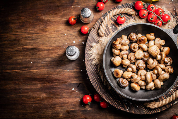 Frying pan with fried mushrooms on a wooden tray. On a wooden background. High quality photo - Photo, image