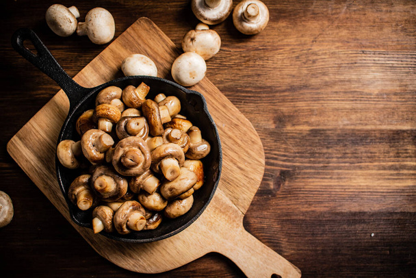 Fried mushrooms in a frying pan on a cutting board. On a wooden background. High quality photo - Photo, Image