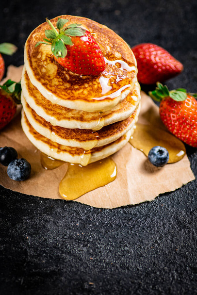 A pile of pancakes with berries and honey. On a black background. High quality photo - Photo, image