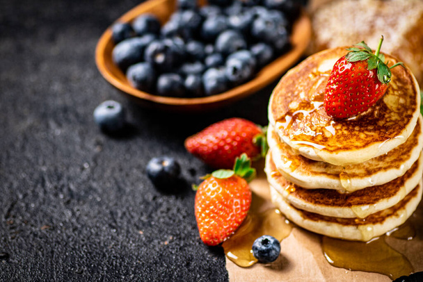 A pile of pancakes with berries and honey. On a black background. High quality photo - Photo, image