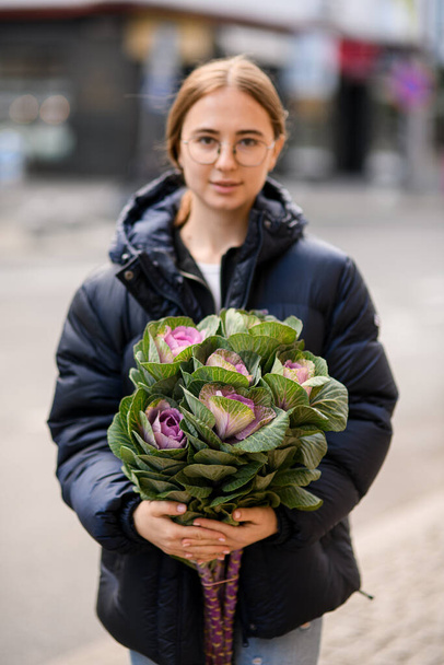 Smiling young woman gently holding large bouquet of beautiful ornamental cabbage brassica in hands. plant for decorating flower arrangements - Foto, Imagem