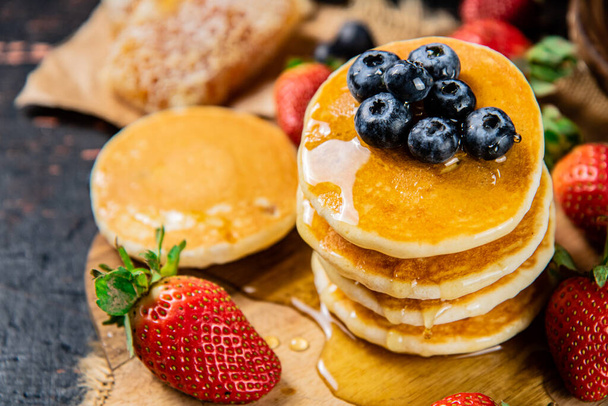 A bunch of pancakes with berries and honey. Against a dark background. High quality photo - Fotografie, Obrázek