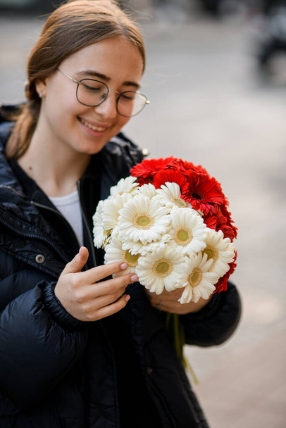 Pretty smiling woman with bouquet of fresh gerbera flowers in her hands. Blurred background. Close-up - Foto, Imagem