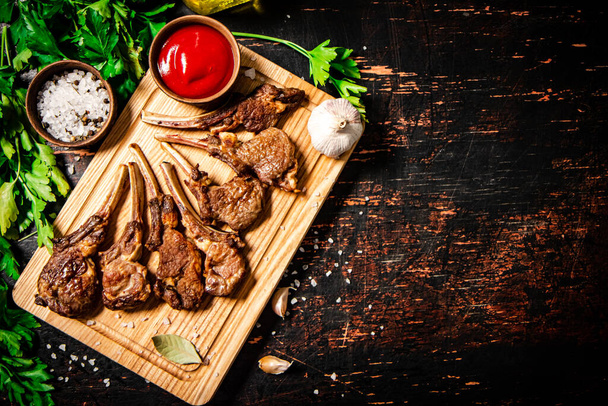 Grilled rack of lamb on a cutting board with parsley and tomato sauce. Against a dark background.  - Фото, зображення