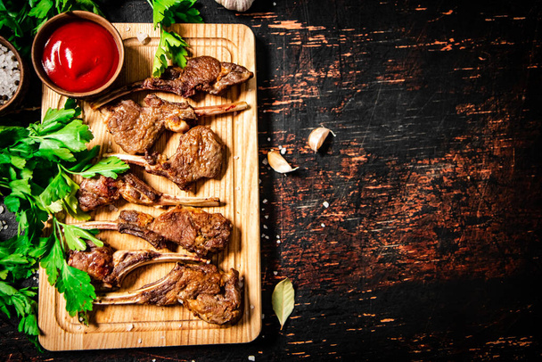Grilled rack of lamb on a cutting board with parsley and tomato sauce. Against a dark background.  - Fotoğraf, Görsel