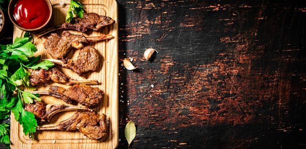 Grilled rack of lamb on a cutting board with parsley and tomato sauce. Against a dark background.  - Fotoğraf, Görsel