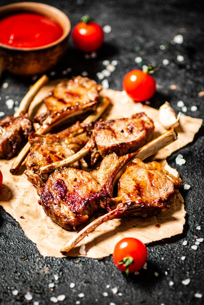 Grilled lamb rack on paper with tomato sauce and cherry tomatoes. On a black background. High quality photo - Фото, зображення