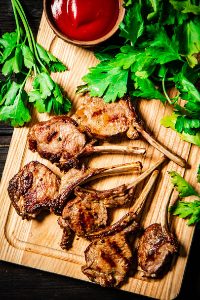 Grilled rack lamb on a cutting board with tomato sauce and parsley. On a wooden background.  - Fotó, kép