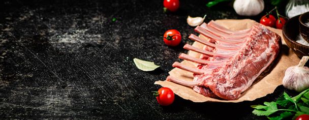 Raw rack of lamb with parsley and tomatoes. On a black background. High quality photo - Fotó, kép