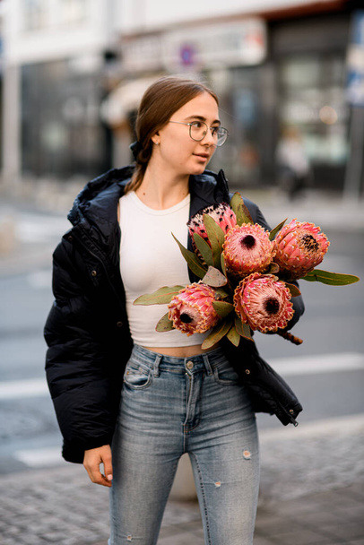 beautiful exclusive bouquet of five pink Protea artichoke flowers in hands of young woman. Girl standing in the street with protea flowers - Valokuva, kuva