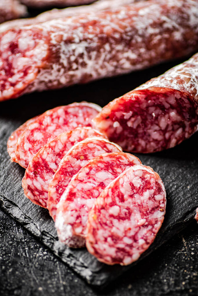 Pieces of salami sausage on a stone board. On a black background. High quality photo - Photo, image