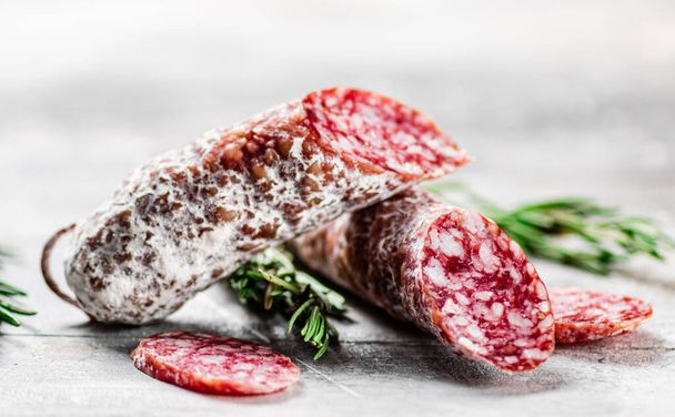 Pieces of salami sausage with sprigs of rosemary. On a gray background. High quality photo - Photo, image