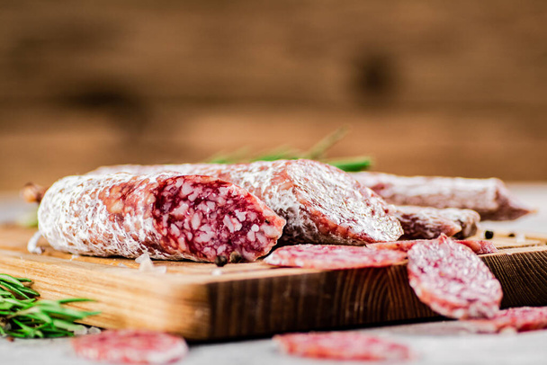Pieces of salami sausage on a cutting board. On a rustic background. High quality photo - Φωτογραφία, εικόνα