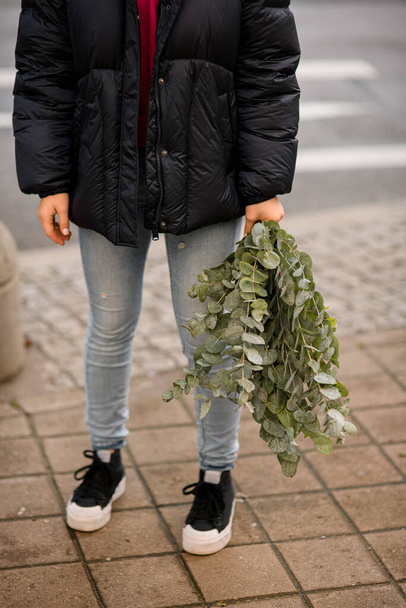 Womans hands hold a bouquet with green eucalyptus branches in the street. plant for decorating bouquets. Flover shop concept - Fotografie, Obrázek