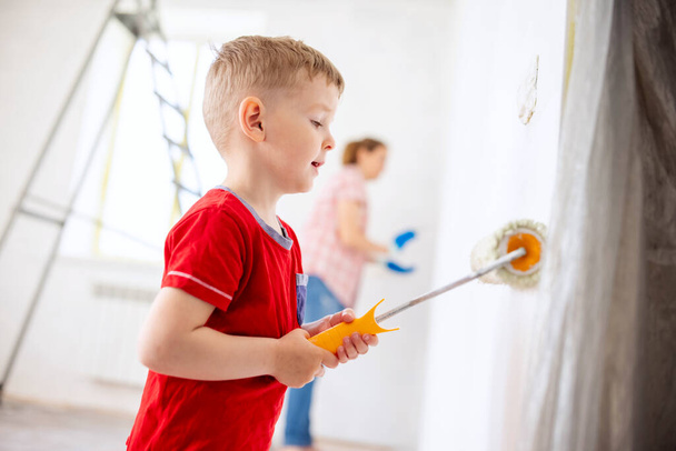 Feliz familia madre e hijo hijo pintar la pared con pintura con rodillo y pincel. Reparación en el apartamento - Foto, Imagen