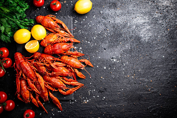 Boiled crayfish with lemon, herbs and tomatoes. On a black background. High quality photo - Fotoğraf, Görsel
