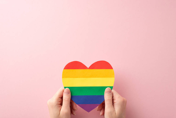 Join the celebration of LGBT History Month with this first person top view empowering image featuring a rainbow heart-shaped card held by woman's hands on pastel pink background - Photo, Image