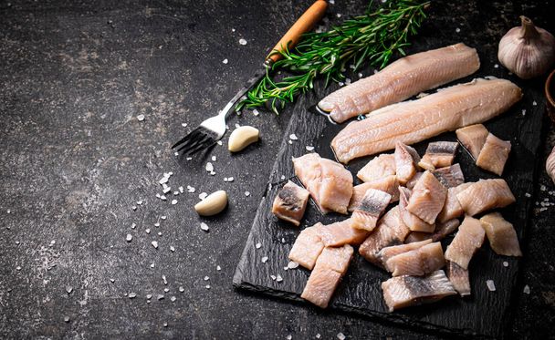 Pieces of salted herring on a stone board with garlic and rosemary. On a black background. High quality photo - Фото, зображення
