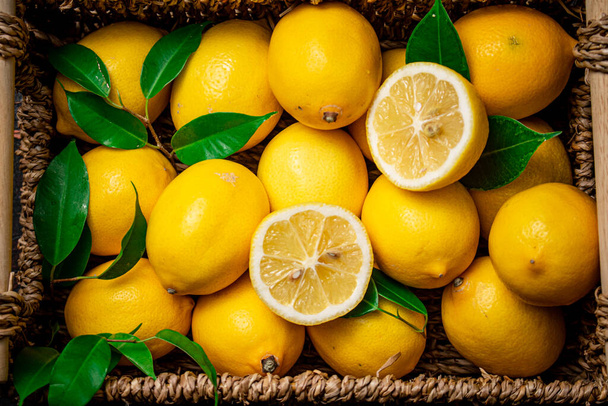 Čerstvé citrony s listím v košíku. Na rustikálním tmavém pozadí. Kvalitní fotografie - Fotografie, Obrázek