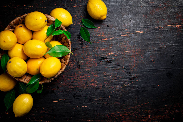 Basket with ripe lemons and leaves. On a rustic dark background. High quality photo - Foto, immagini