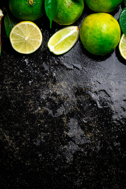 Pieces and whole lime with leaves. On a black damp background. High quality photo - Zdjęcie, obraz