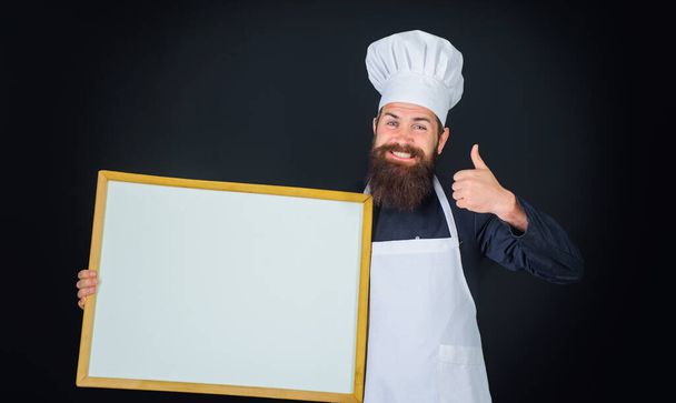 Smiling male chef, cook or baker with blank board showing thumb up. Chef in uniform with empty menu blackboard. Blank billboard for advertising text menu in kitchen and restaurant. Cooking and food - Foto, immagini