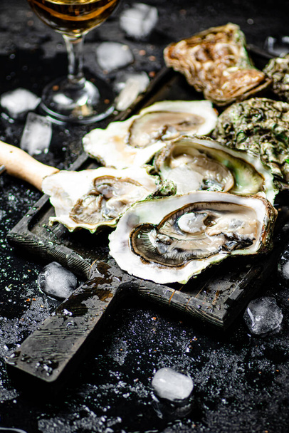 Raw oysters with ice on an cutting board. On a rustic dark background. High quality photo - Zdjęcie, obraz