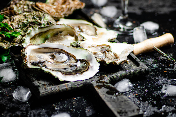 Raw oysters with ice on an cutting board. On a rustic dark background. High quality photo - Zdjęcie, obraz