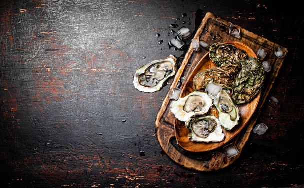 Fresh oysters with ice on a wooden plate. Against a dark background. High quality photo - Φωτογραφία, εικόνα