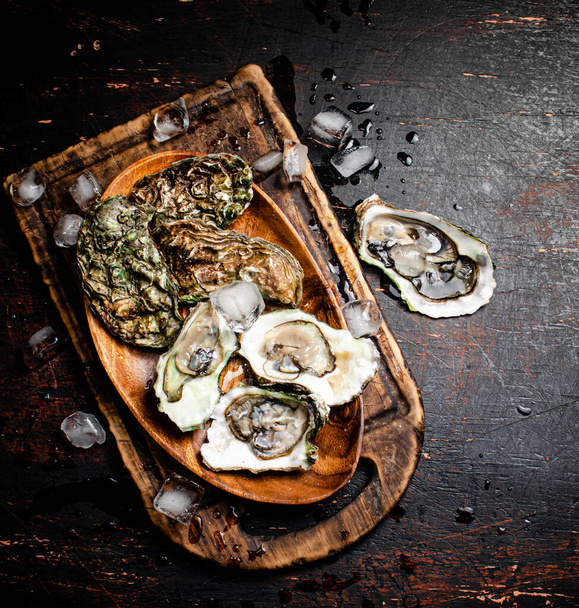 Fresh oysters with ice on a wooden plate. Against a dark background. High quality photo - Foto, Imagen