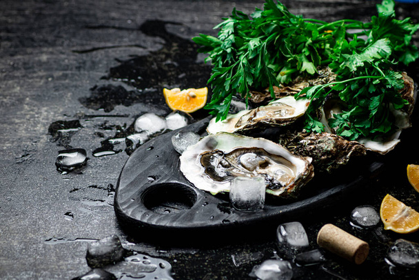 Fresh oysters on a cutting board. On a black background. High quality photo - Foto, afbeelding