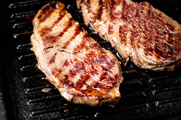 Aromatic grilled steak in a frying pan. Against a dark background. High quality photo - Foto, afbeelding