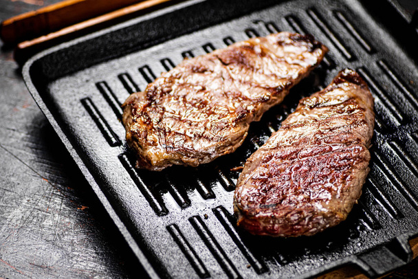 Aromatic grilled steak in a frying pan. Against a dark background. High quality photo - Fotoğraf, Görsel