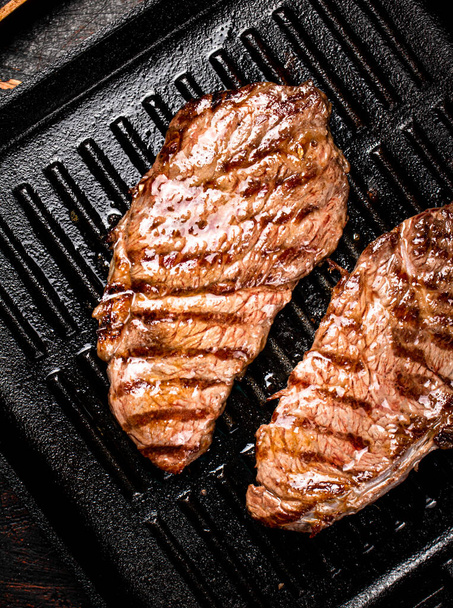 Aromatic grilled steak in a frying pan. Against a dark background. High quality photo - Fotografie, Obrázek