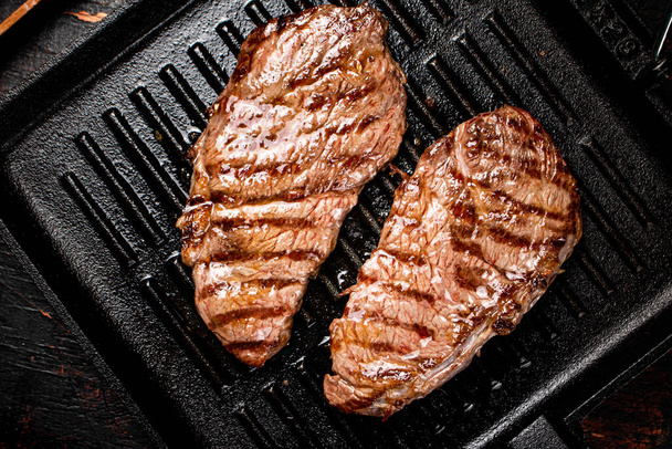 Aromatic grilled steak in a frying pan. Against a dark background. High quality photo - Fotoğraf, Görsel