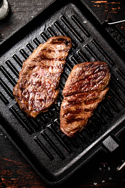 Aromatic grilled steak in a frying pan. Against a dark background. High quality photo - Foto, Imagem