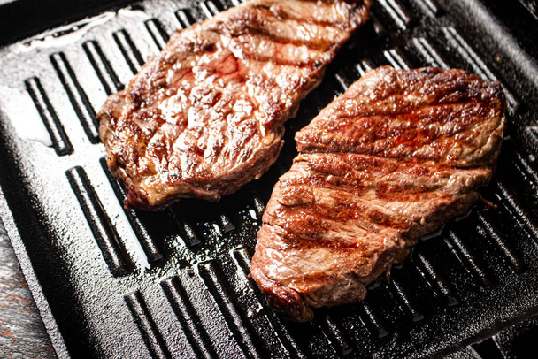 Aromatic grilled steak in a frying pan. Against a dark background. High quality photo - 写真・画像