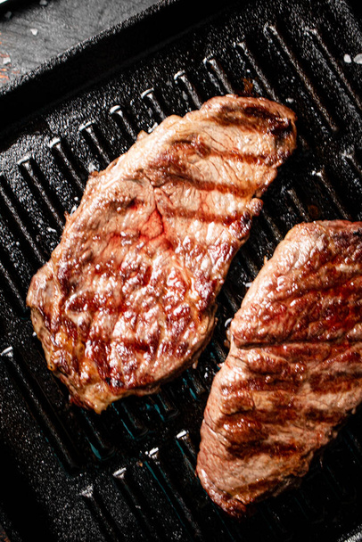 Aromatic grilled steak in a frying pan. Against a dark background. High quality photo - Фото, изображение