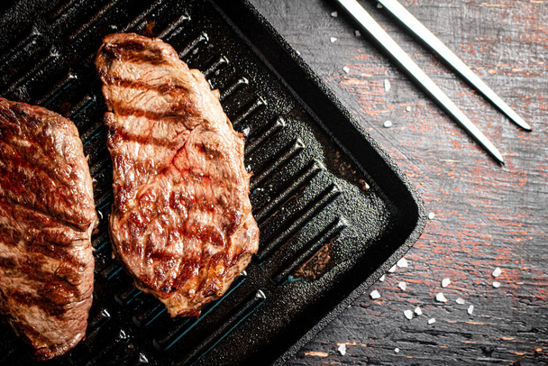 Aromatic grilled steak in a frying pan. Against a dark background. High quality photo - Valokuva, kuva