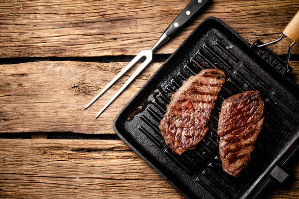 Grilled steak in a frying pan. On a wooden background. High quality photo - 写真・画像